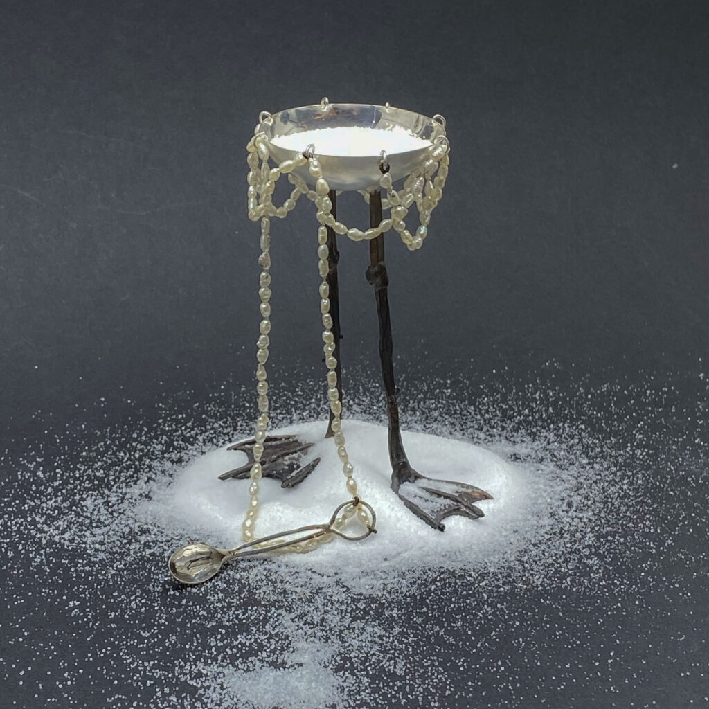 Finurlig sockerskål av silver med fötter i gjutet brons och en sked som hänger i en collier av sötvattenspärlor. skapad av Judit Fritz.